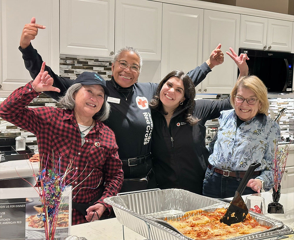 A Red Cross volunteer and Three Tiffany Circle memberspose for picture in a kitchen with food on the table at the Fisher House.