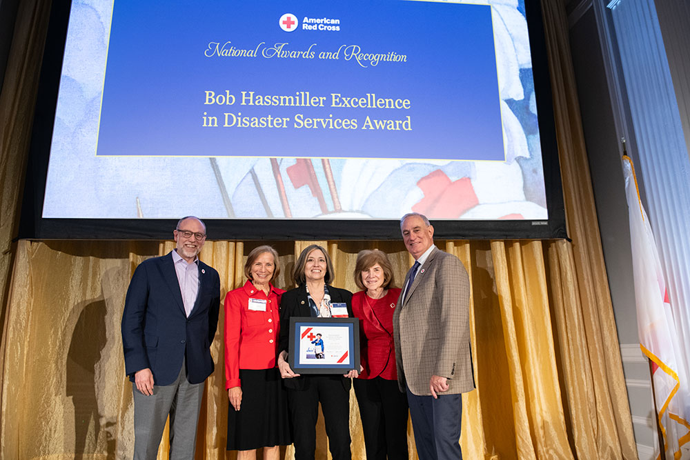 Jody Kimbrel with four Red Cross staff members on stage smiling while holding a framed Red Cross award.