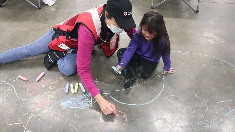 A Red Cross disaster mental health volunteer draws with chalk on the ground with a four-year-old staying at a shelter in Watsonville, Calif.