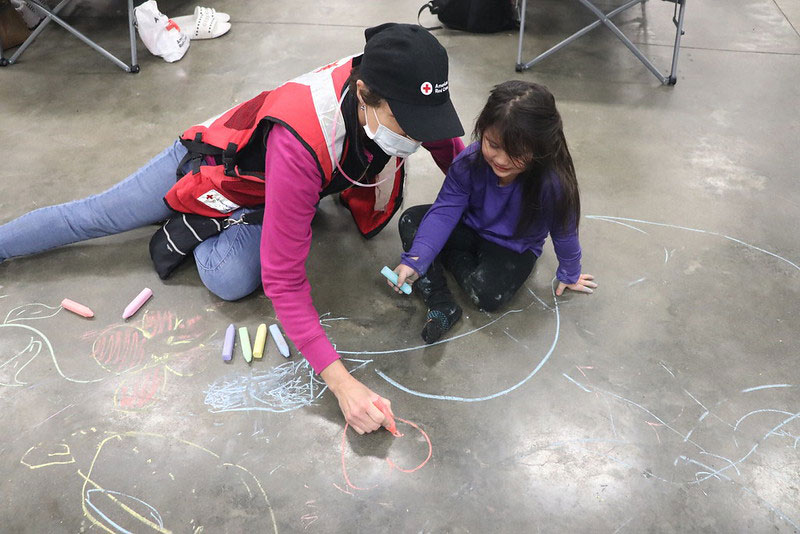 A Red Cross disaster mental health volunteer draws with chalk on the ground with a four-year-old staying at a shelter in Watsonville, Calif.