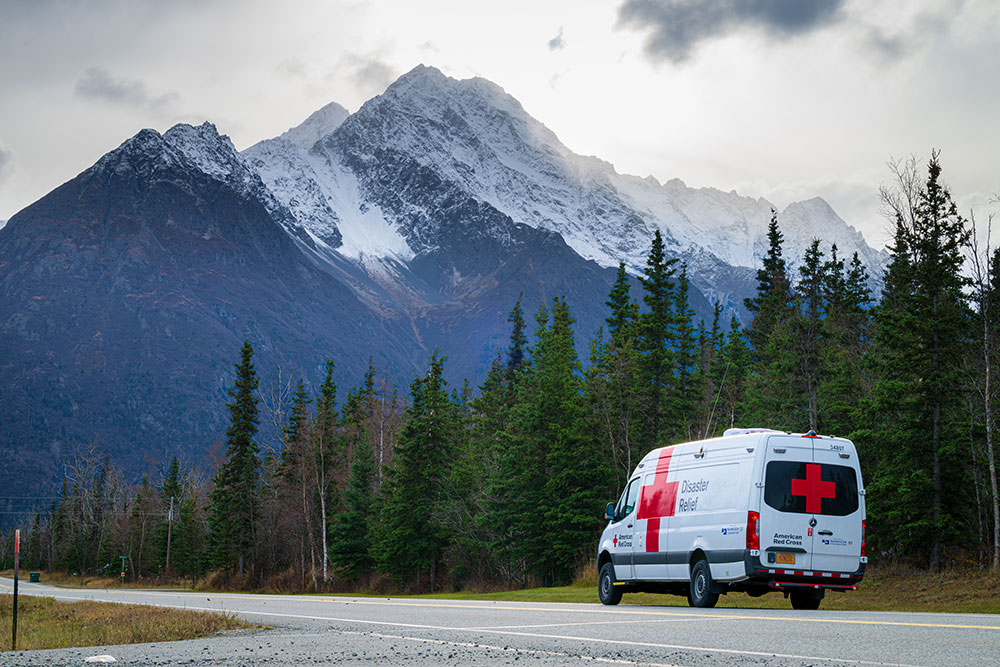 Red Cross Disaster Relief van on the road next to tall trees and a snowy mountain.