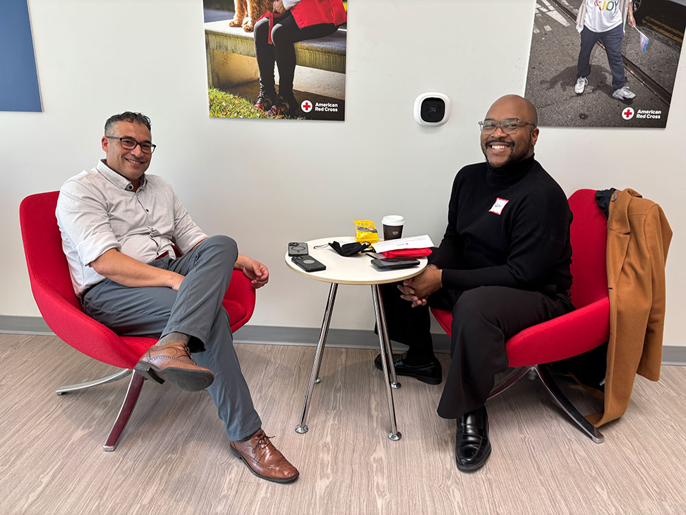 Ed Faso and Noah James sitting in chairs with a small round table between them, at the Red Cross blood laboratory in San Leandro