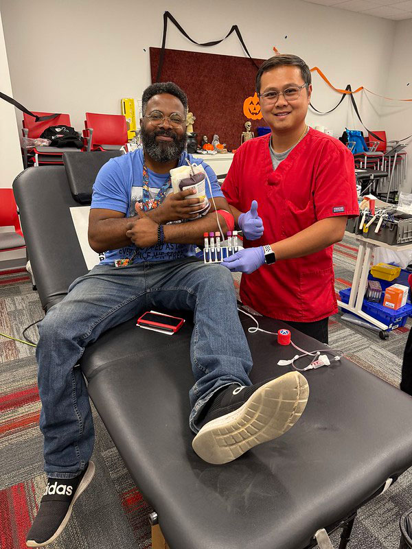 blood donor sitting in chair after dontating blood with a nurse next to him. Both are giving a thumbs up.