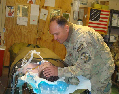Pastor Riley praying over a wounded service member in bed with breathing tube in Afghanistan.