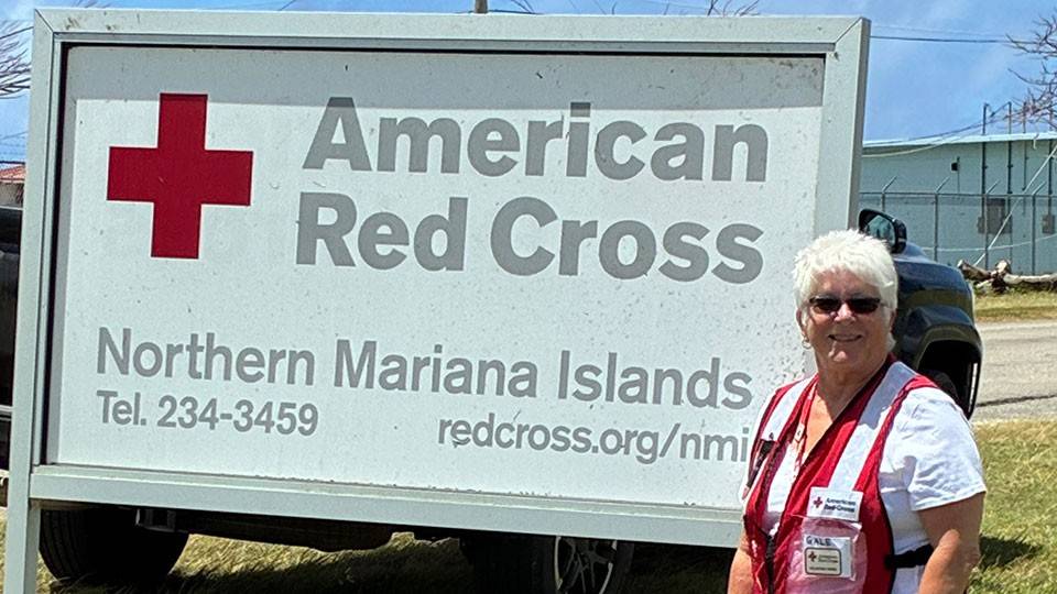 Red Cross volunteer Gale Carli in Saipan standing on the grass in front of the American Red Cross Northern Mariana Islands sign.
