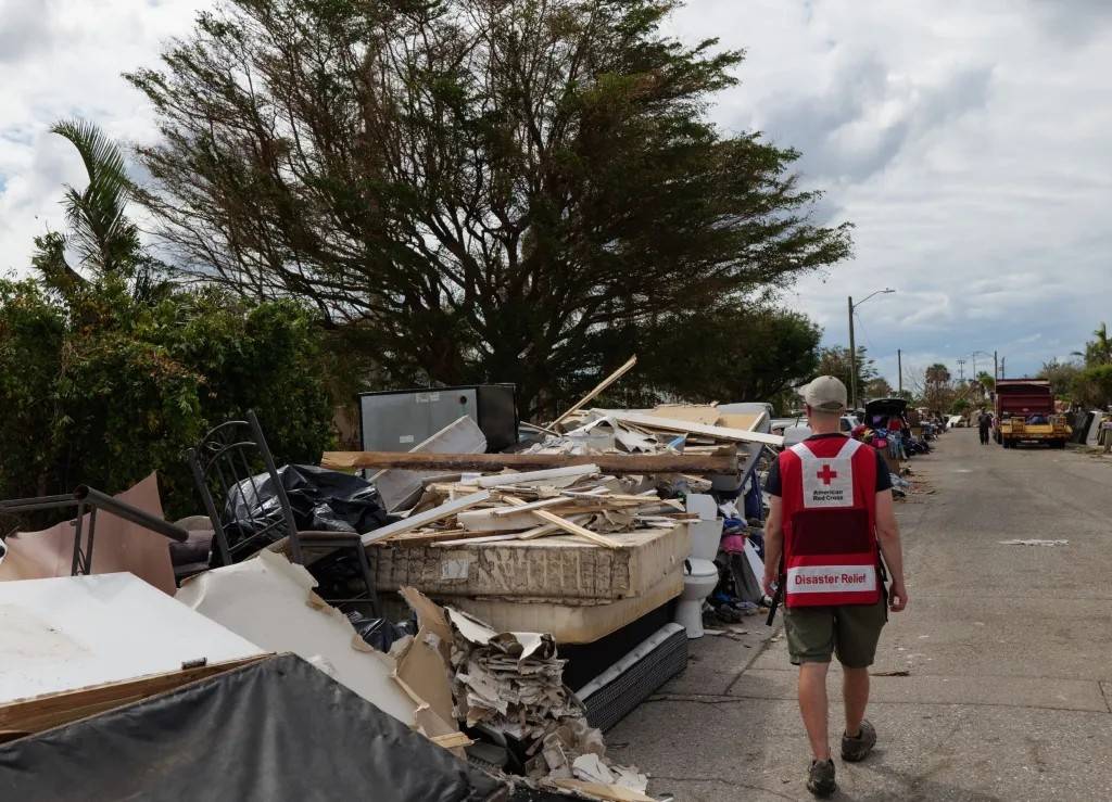 A Red Crosser walks down a street lined with wet furniture, appliances and personal items removes from people’s homes after Hurricane Ian. Photo by Jodi Long/American Red Cross. October 9, 2022.