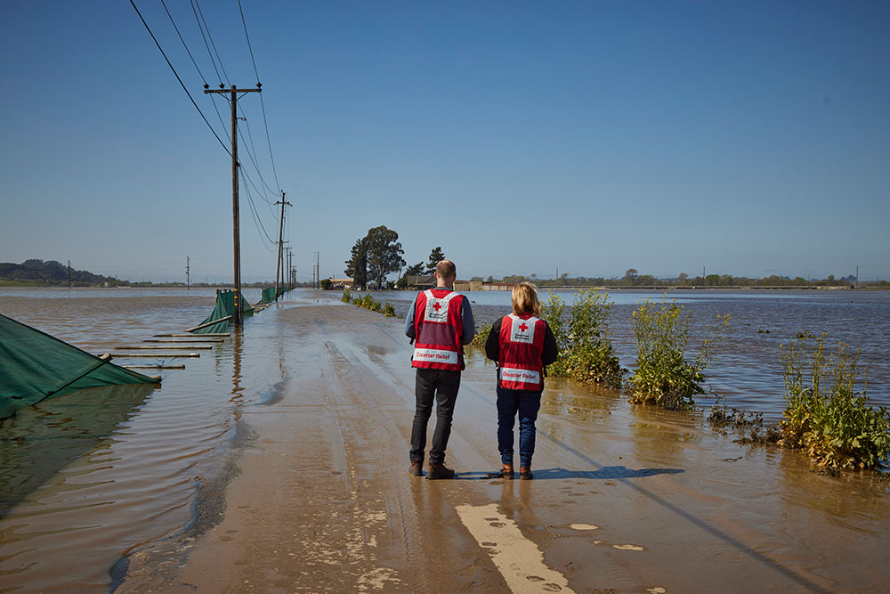 Red Cross volunteers standing on long open road with flood waters all around.