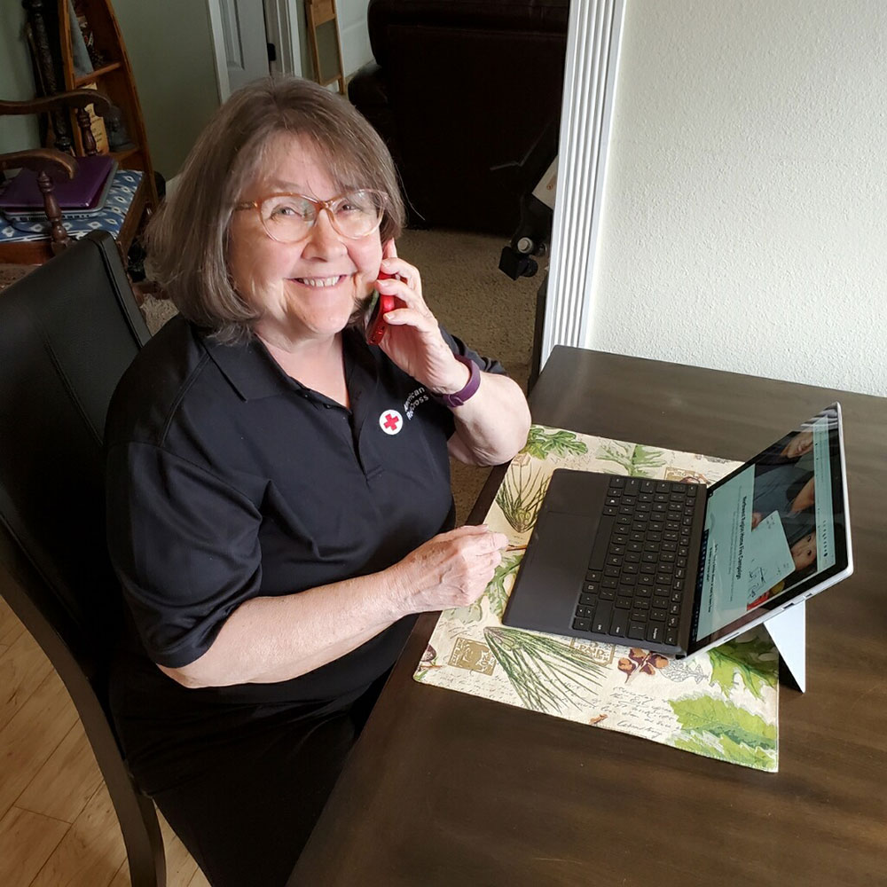 American Red Cross volunteer Kathy Kennard speaking on a phone while sitting at a desk with a laptop.