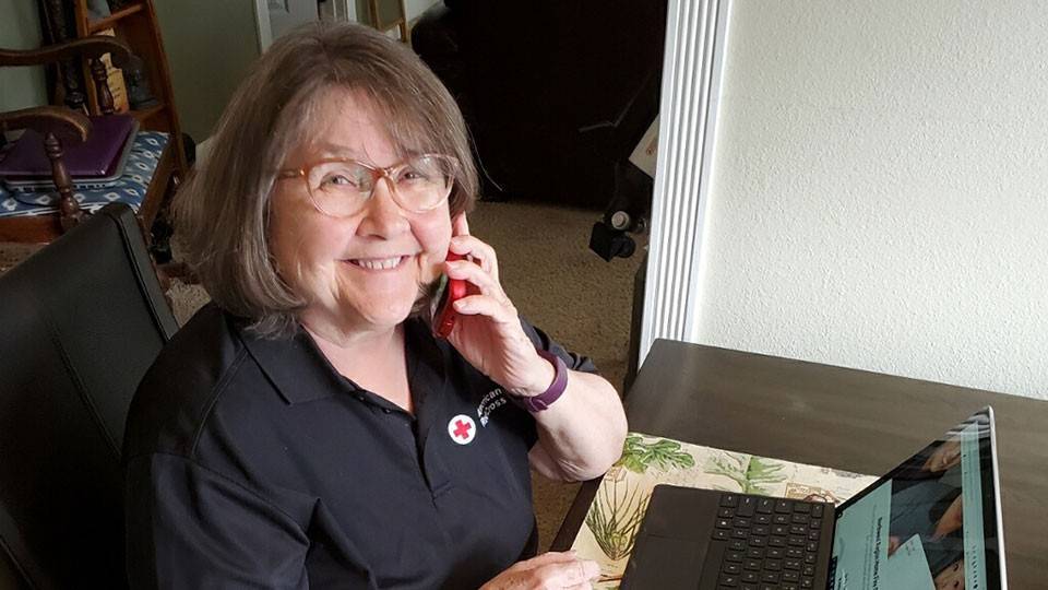 American Red Cross volunteer Kathy Kennard speaking on a phone while sitting at a desk with a laptop.