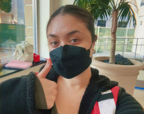 Red Cross volunteer wearing mask and Red Cross vest takes a selfie while giving a thumbs up.
