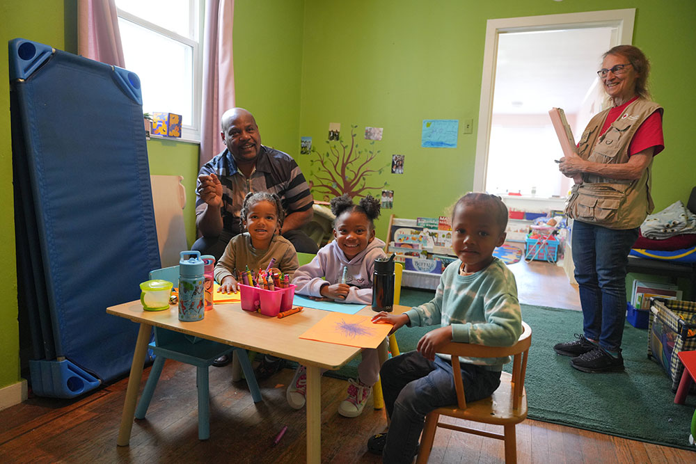 Red Cross volunteer in a room with an adult and kids who are coloring on a small table.