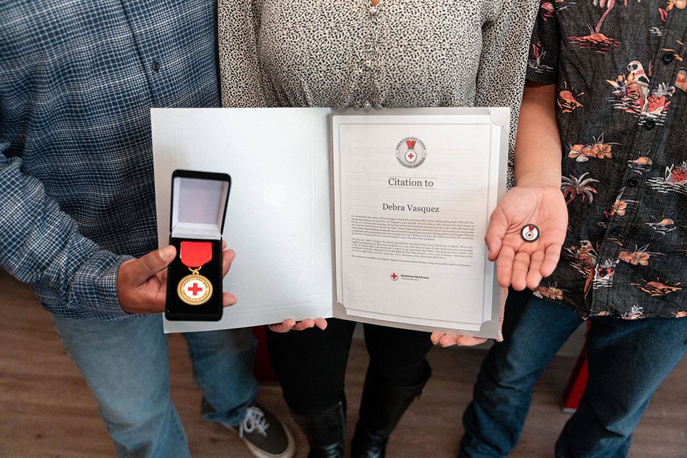Philip, Debbie, and Andrew holding Debbie’s award which includes a medal, a certificate, a citation, and a lapel pin.