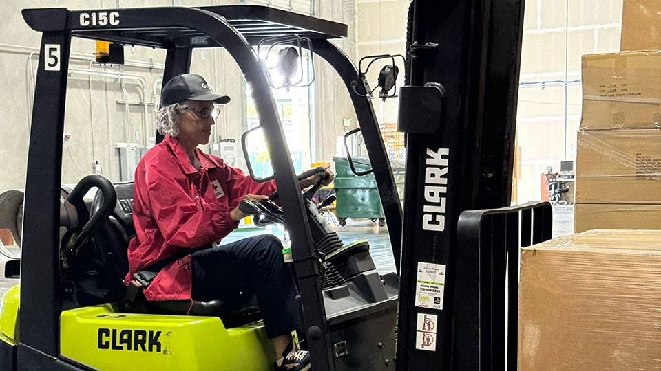 Lyra Kelly driving a forklift in order to get supplies delivered to families in need.