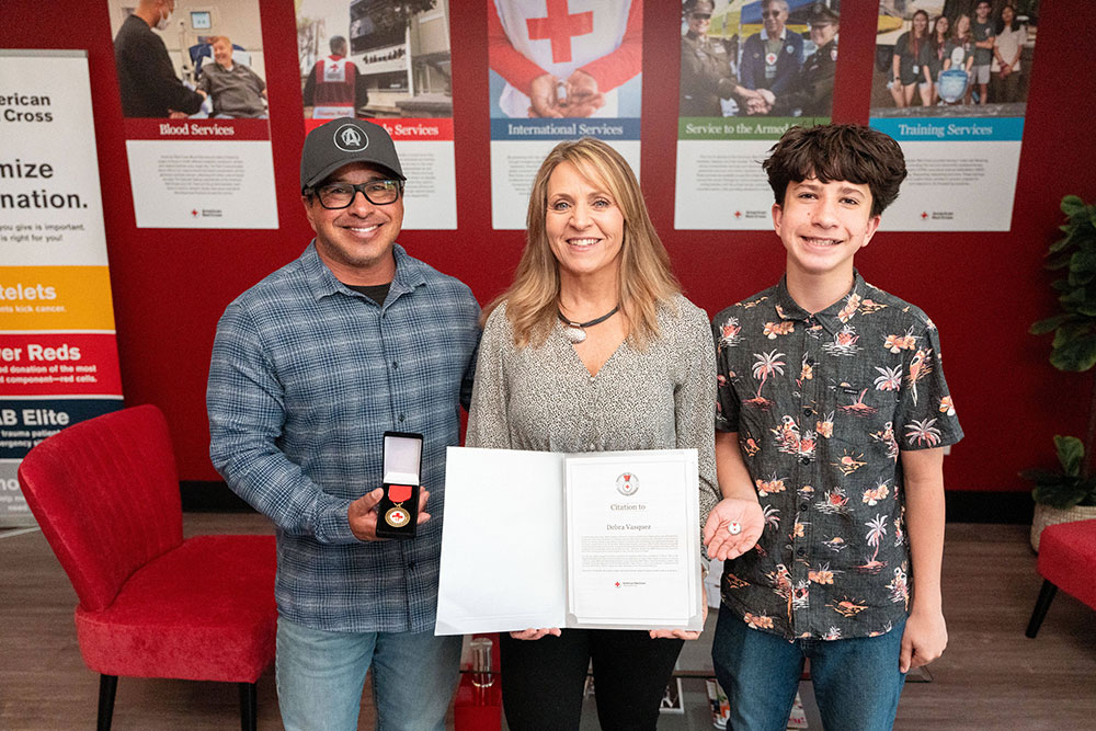 Philip, Debbie, and Andrew holding Debbie’s award which includes a medal, a certificate, a citation, and a lapel pin.