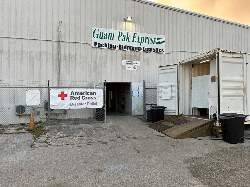 Outside of Guam Pak Express warehouse with Red Cross banner hanging on a fence