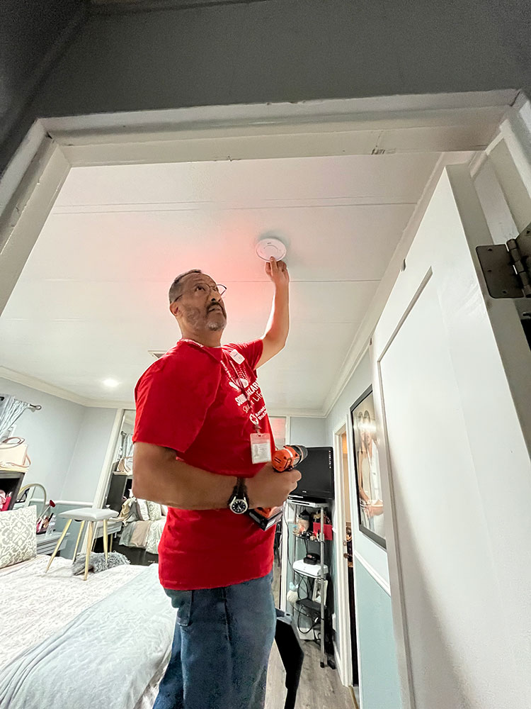 Red Cross volunteer installing a smoke alarm on a ceiling.