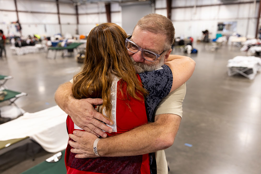 Red Cross volunteer hugs disaster victim in a shelter.