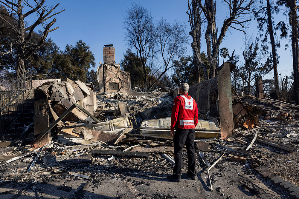 Red Cross volunteer standing next to burned down house.