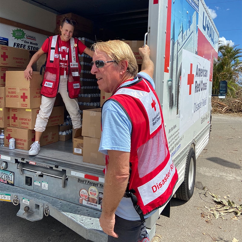 2 Red Cross volunteers in back of moving van with Red Cross boxes