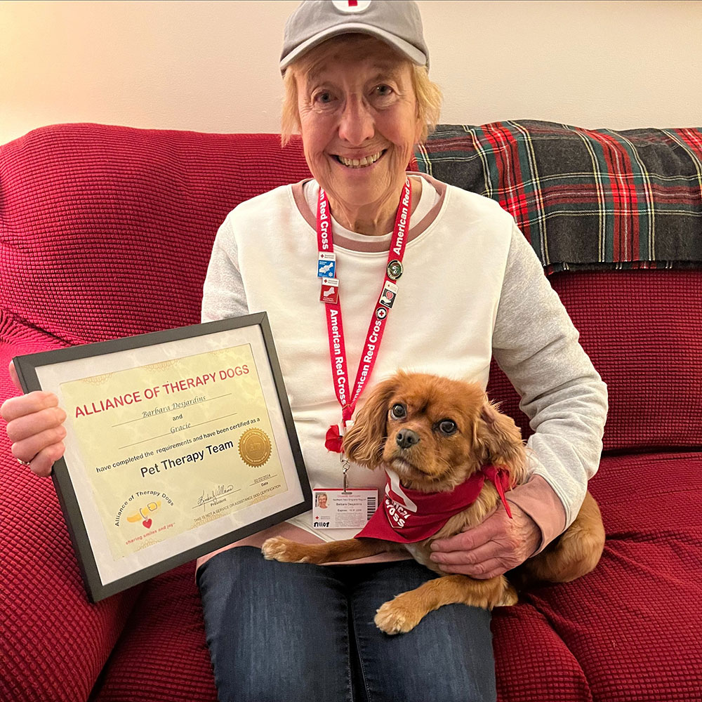 Barbara Desjardins and therapy dog Gracie sitting on a couch while displaying Barbara's Red Cross awards.