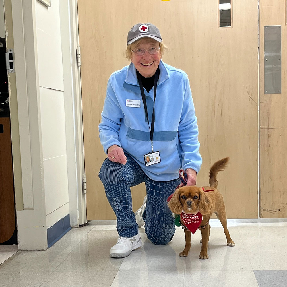 Barbara Desjardins kneeling next to therapy dog Gracie.