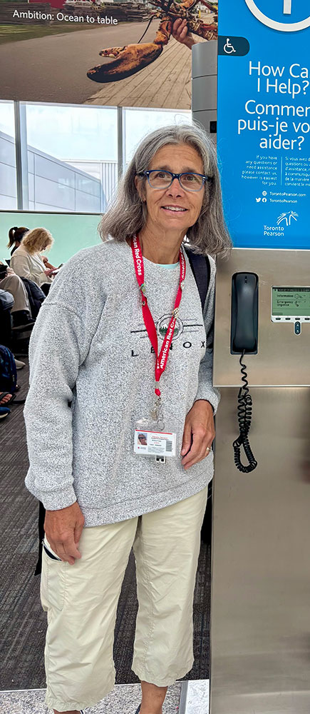 Brenda Foley with Red Cross lanyard around neck and standing next to a phone in an airport.