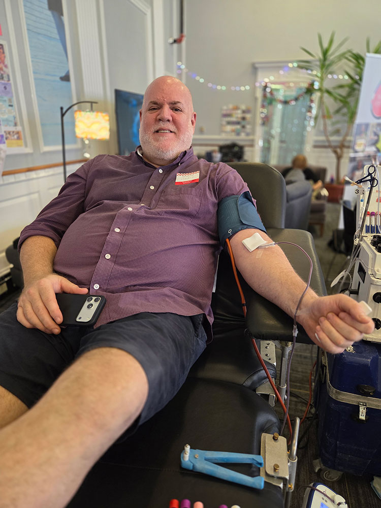 Chris O’Connor sitting in a blood donation chair and donating blood.