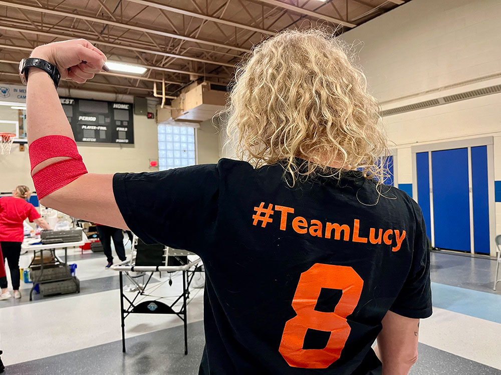 Chrissy Bellemare wearing a team Lucy t-shirt with red bandage around arm at a blood drive.