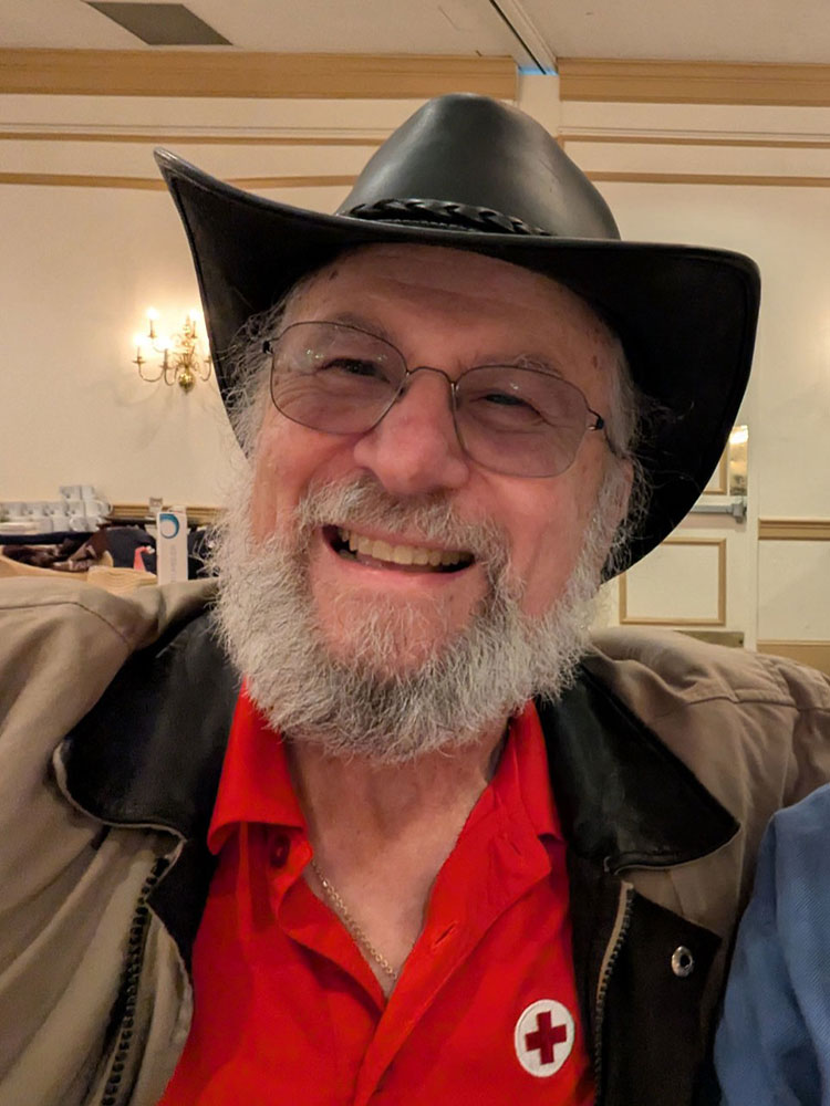 David Punia smiling with a beard and glasses wearing a cowboy hat and red cross shirt.