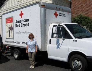 Deb Camejo stands smiling in front of a parked American Red Cross blood services truck.