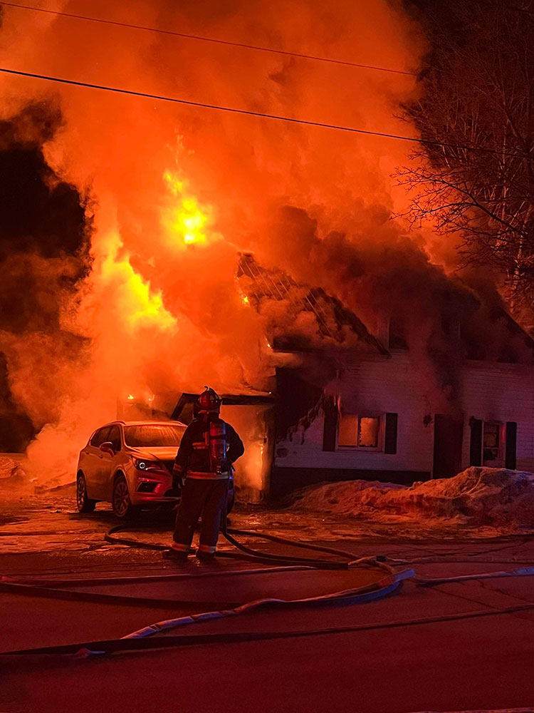 firefighter with hose in front of a house that's on fire.