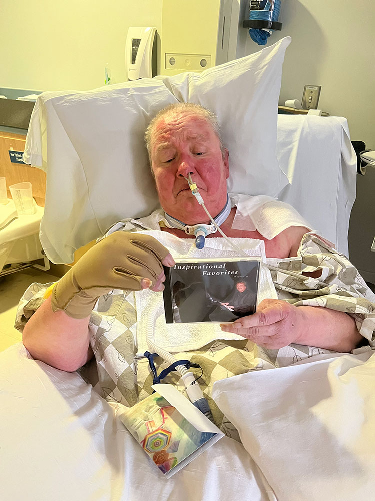 Diana Levesque in hospital bed with breathing tube and holding a CD case.