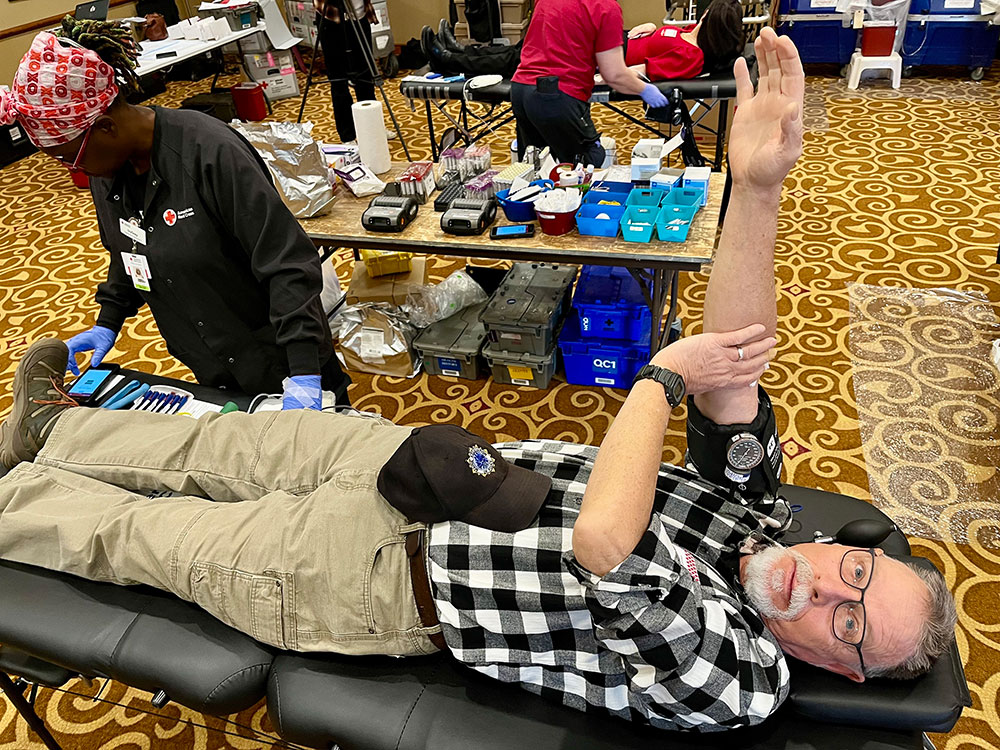 Ivy Grey Robinson wearing head wrap, glasses and Red Cross jacket, works on blood donor lying on a cot.