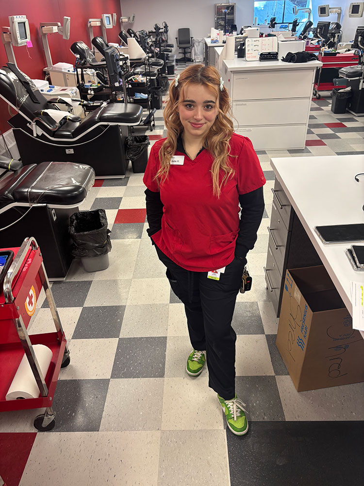 Jade Howard, wearing a Red Cross shirt and name tag, at a blood donation center.