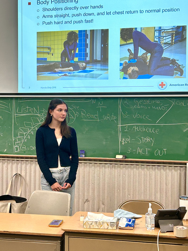 Kate Morrison standing at the front of a classroom with a projector showing CPR training.