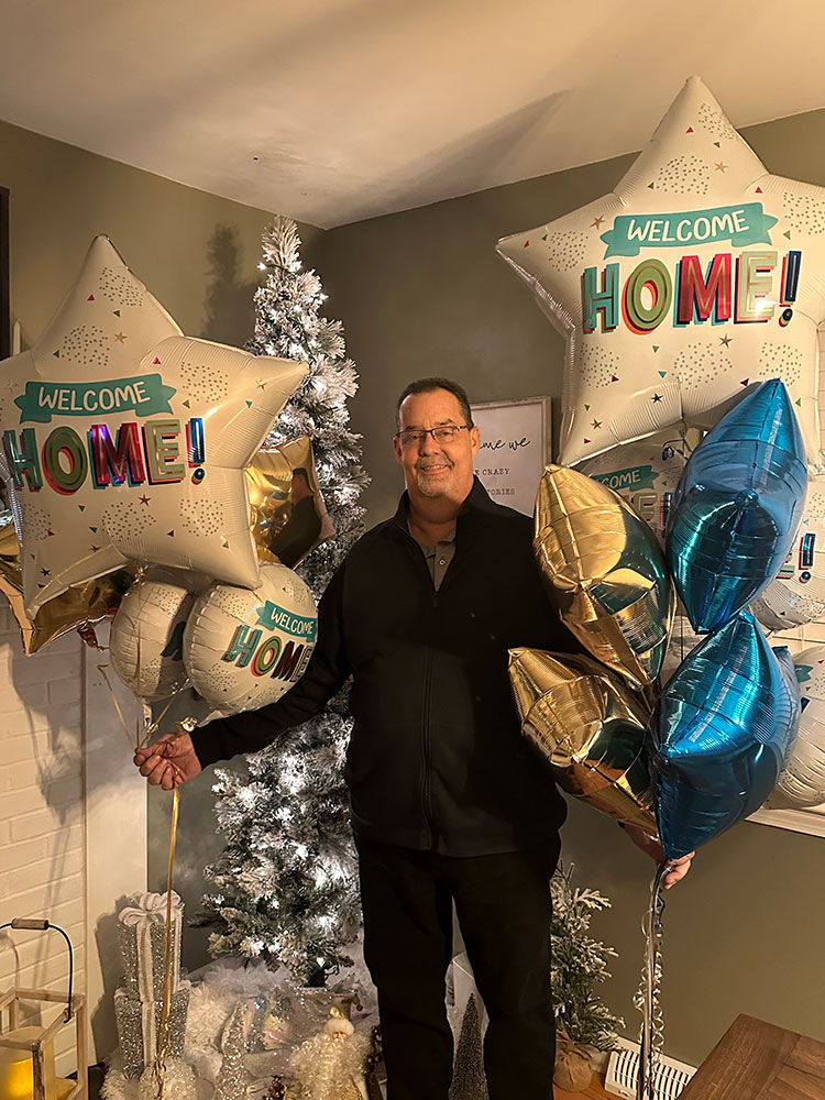 Keith Deavitt standing in a room next to multiple balloons the say welcome home!