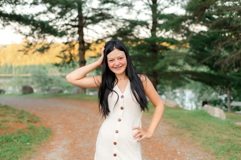 Lilly Chamber in white dress and trees and lake in background