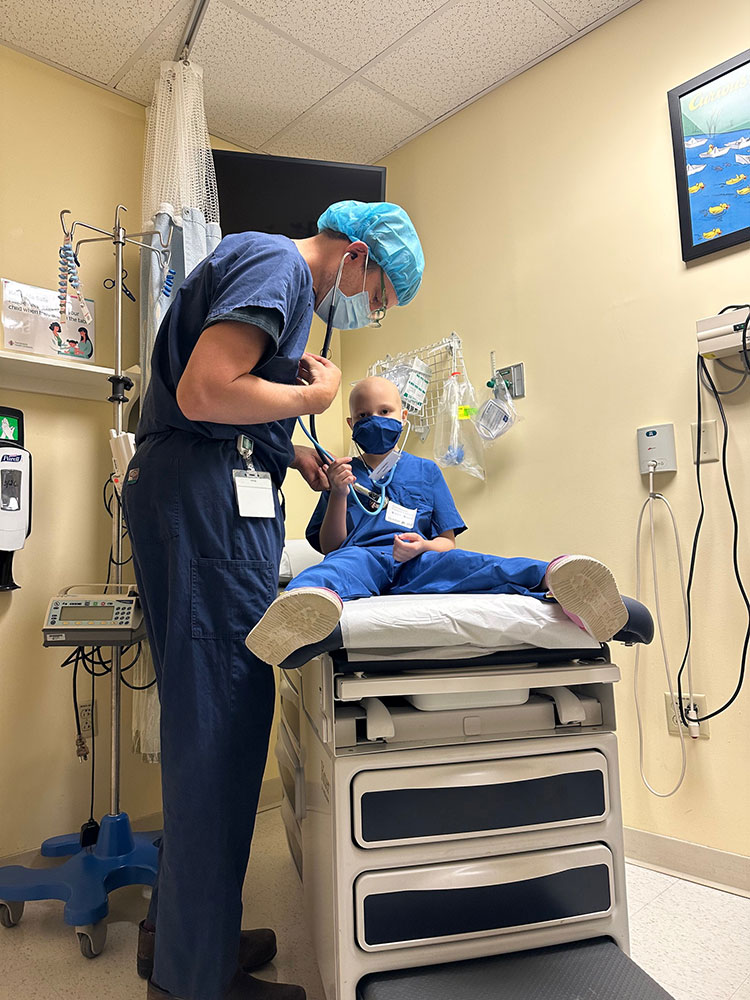 Lucy Bellemare sitting on exam table while a doctor shows Lucy how to use a stethoscope.