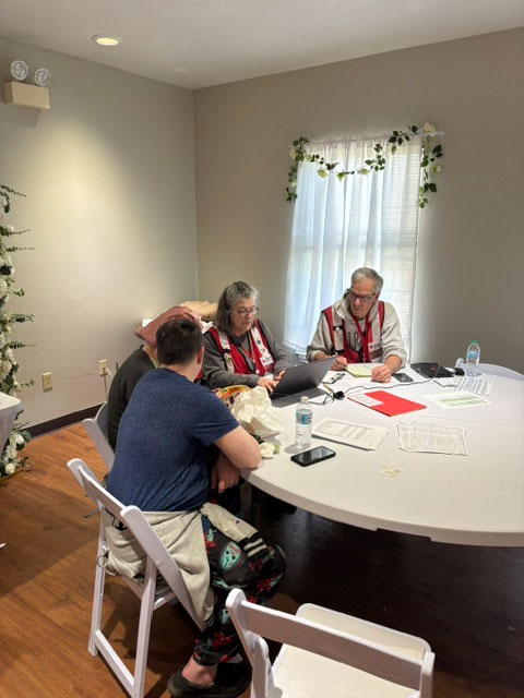 red cross volunteers and residents sitting at a table with paperwork spread out.