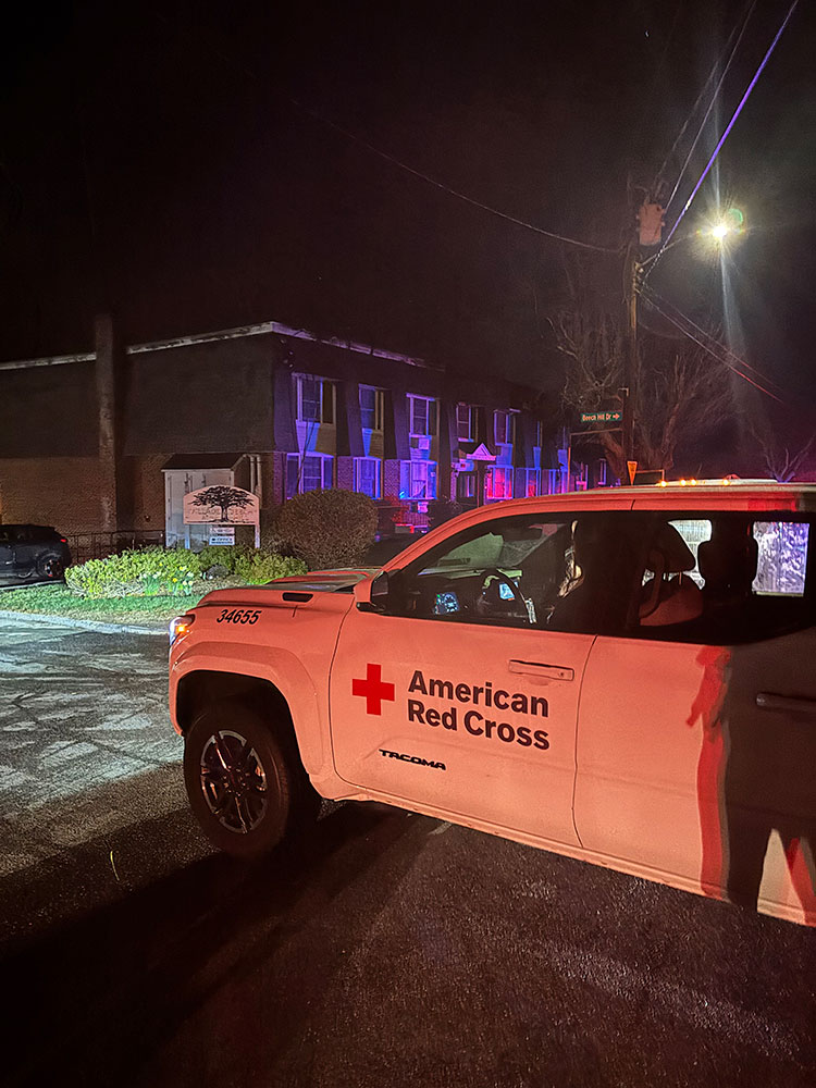 a Red Cross truck parked in front of an apartment building at night.