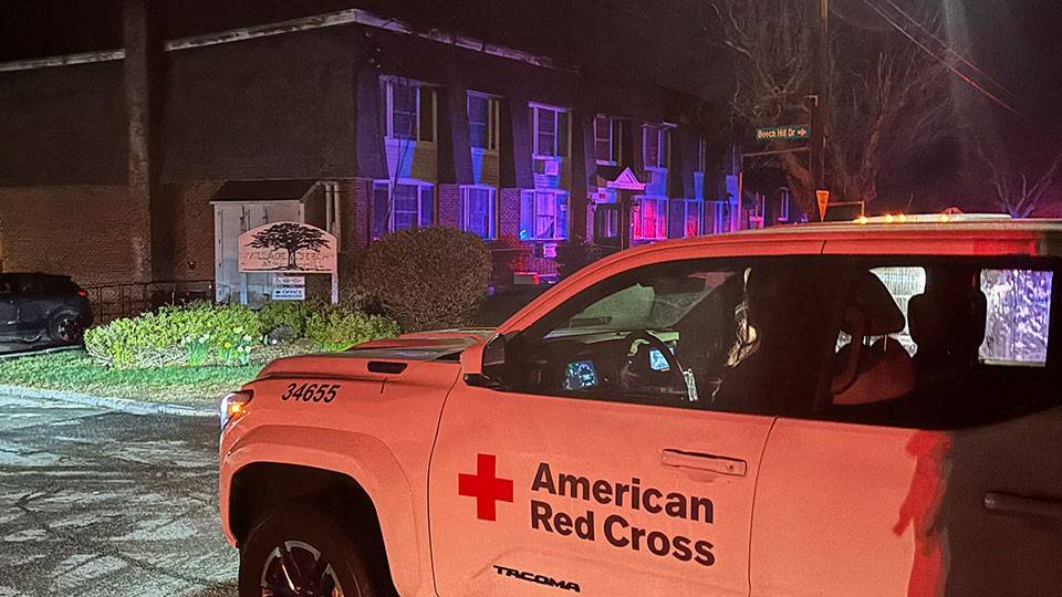 a Red Cross truck parked in front of an apartment building at night.