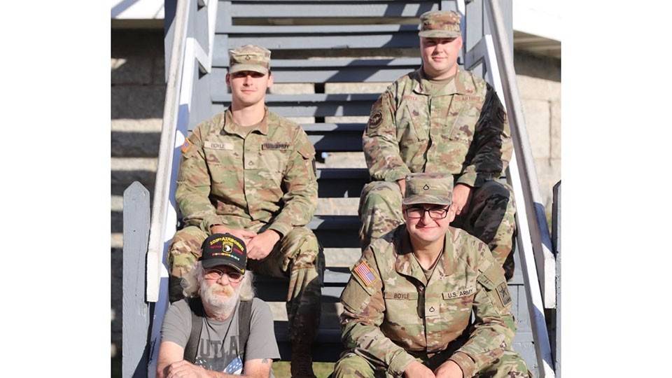 four people sitting on a staircase. Three of them in military camouflage clothing and one wearing a 101st airborne hat.