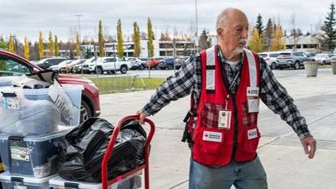 Paul Miller wearing a Red Cross vest while pulling a cart full of containers.