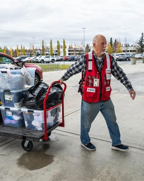 Paul Miller wearing a Red Cross vest while pulling a cart full of containers.