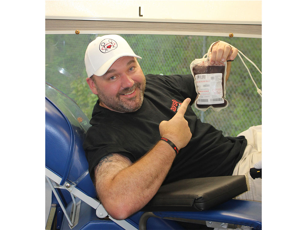Ray Poulin sitting on cot hold bag of blood and pointing at it.