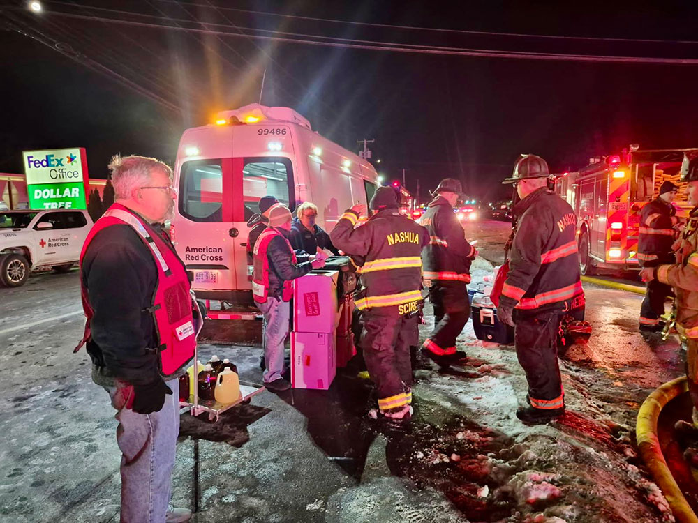 Red Cross volunteers and firefighters standing by a Red Cross van on a snowy road.