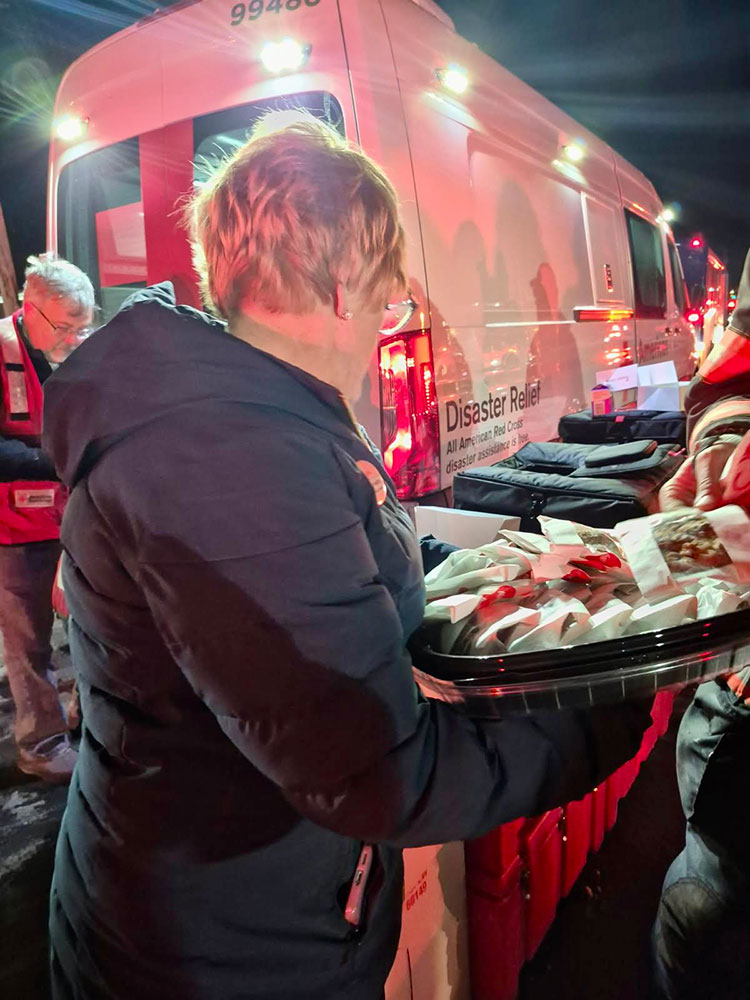 Red Cross volunteers handing out food by a Red Cross van on a snowy road.