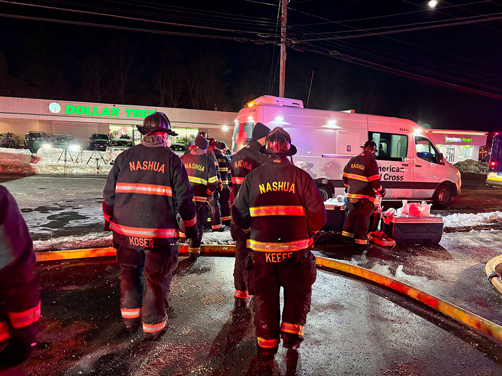 Firefighters standing by a Red Cross van on a snowy road.
