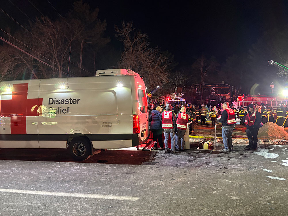 Red Cross volunteers and firefighters standing by a Red Cross van on a snowy road.