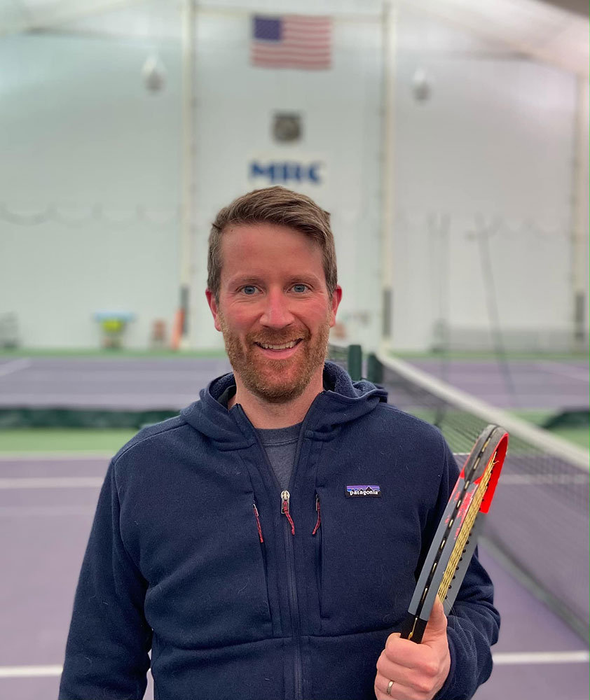 Seth Meyer on tennis court holding a tennis racket.